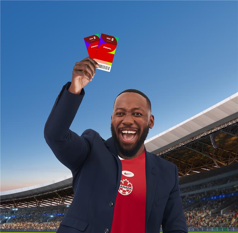 A man wearing a soccer jersey and a dark jacket stands in a stadium, holding two Visa tickets in the air and smiling at the camera.